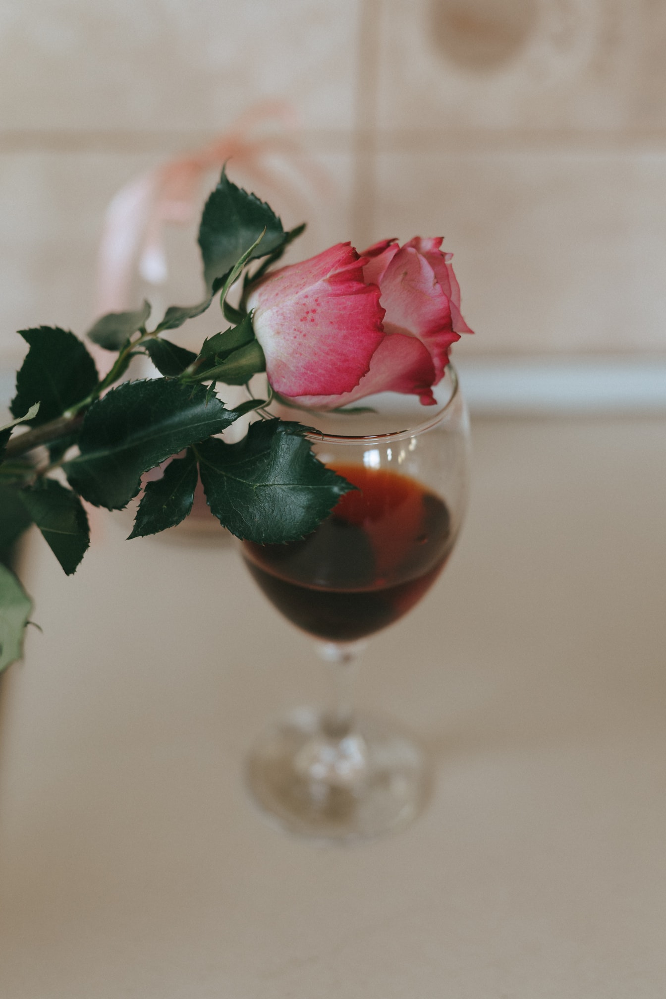 Pupoljak ružičaste ruže na čaši crnog vina izbliza