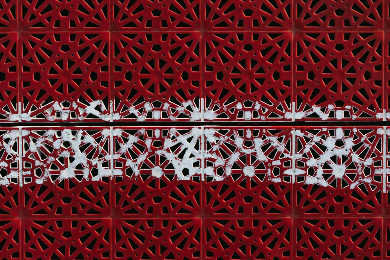 Witte verf over donkerrood plastic met geometrisch arabesk patroon