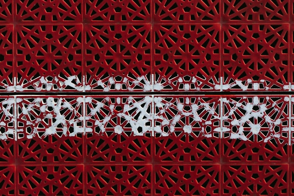 Vernice bianca su plastica rosso scuro con motivo geometrico arabescato