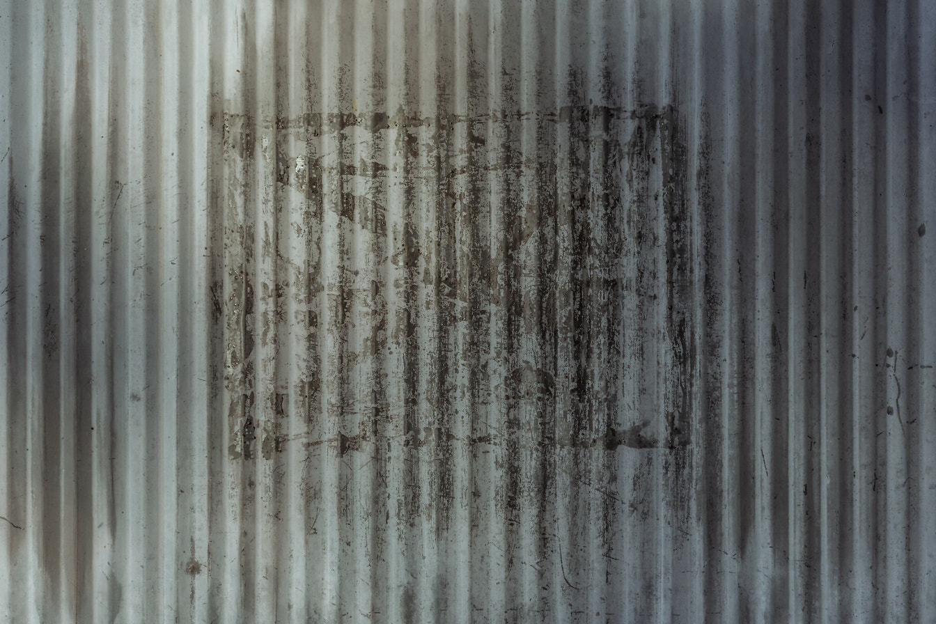 Sivý kovový povrch so zvislými čiarami a čiernymi graffiti