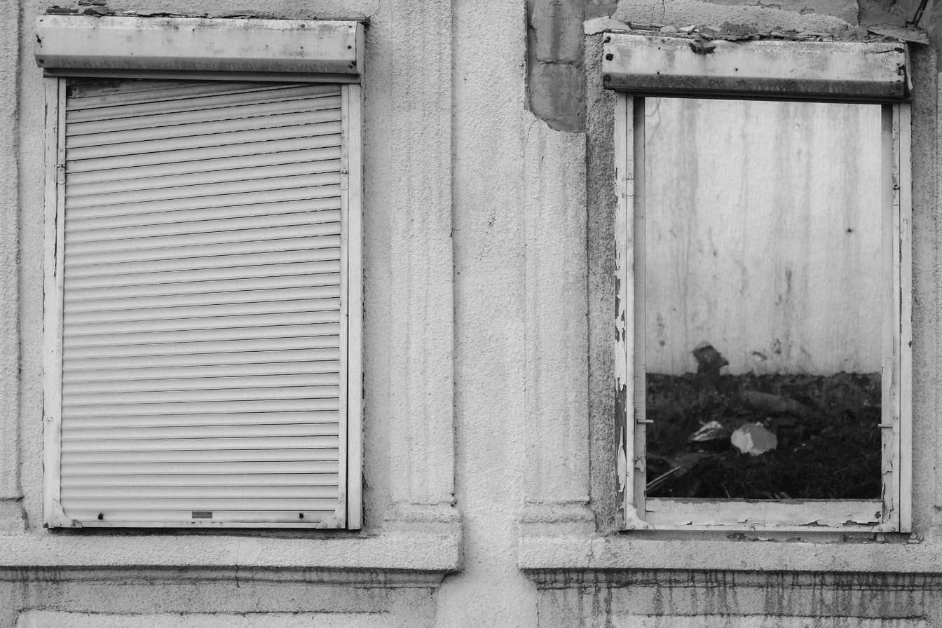 Fotografia em preto e branco de janelas em decomposição em uma casa abandonada