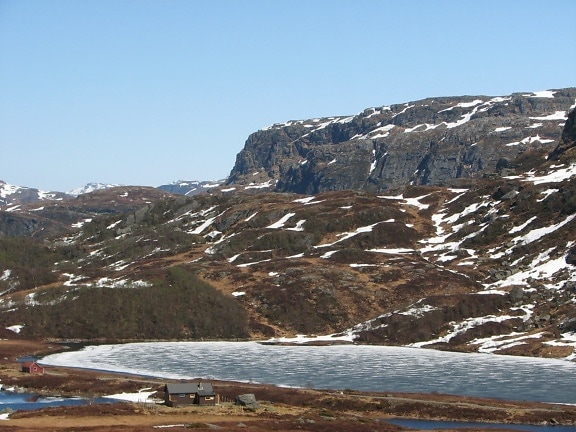 Dům na kopci se zamrzlým jezerem a horami v pozadí