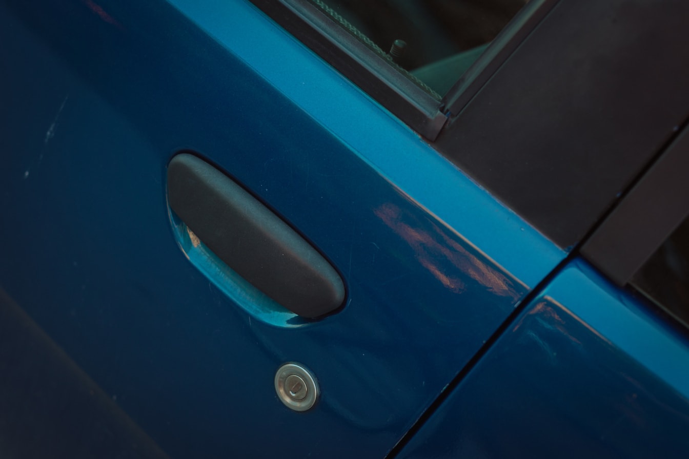 Nærbillede af et bildørhåndtag på mørkeblå bil
