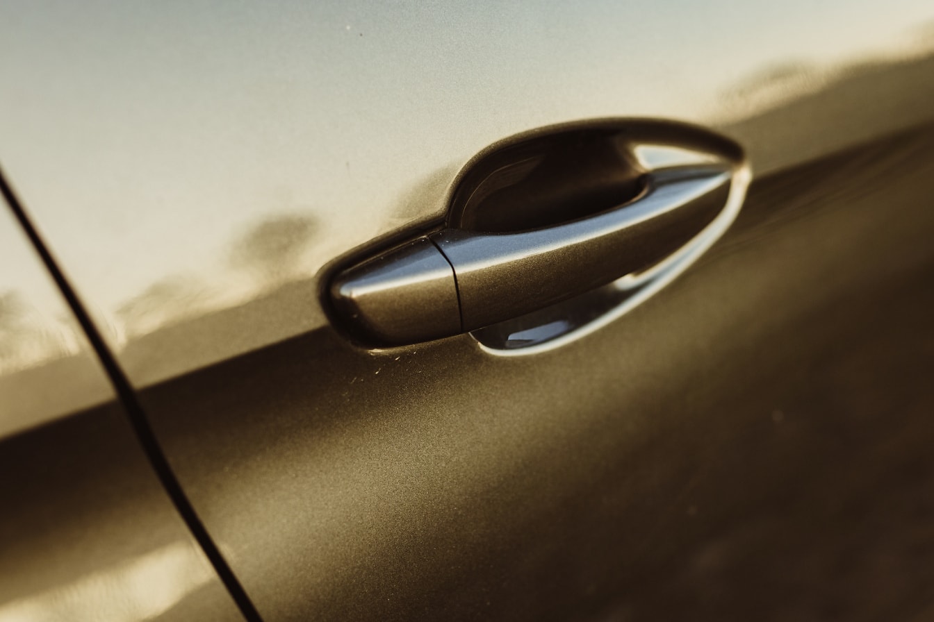 Prim-plan al mânerului ușii unei mașini cu reflexie aurie a strălucirii
