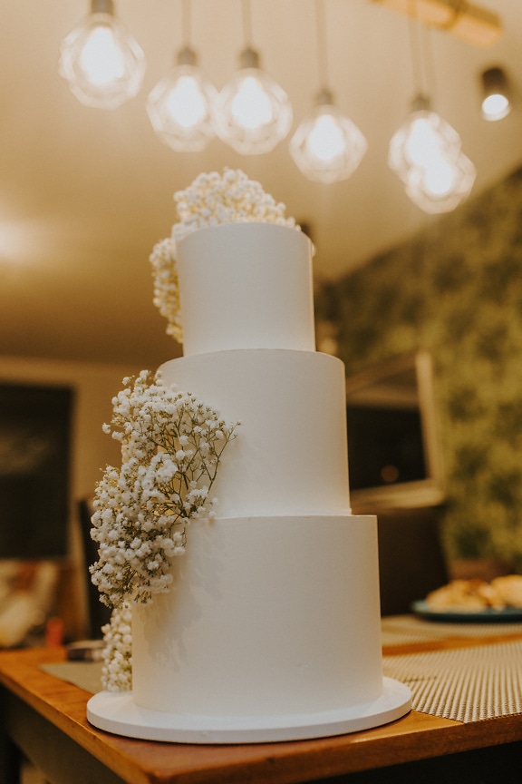 เค้กแต่งงานสีขาวสามชั้นพร้อมดอกไม้ด้านบน
