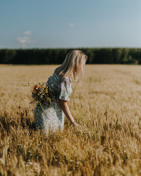 Ung kvinna på landsbygden som rymmer en bukett av blommor i ett vetefält