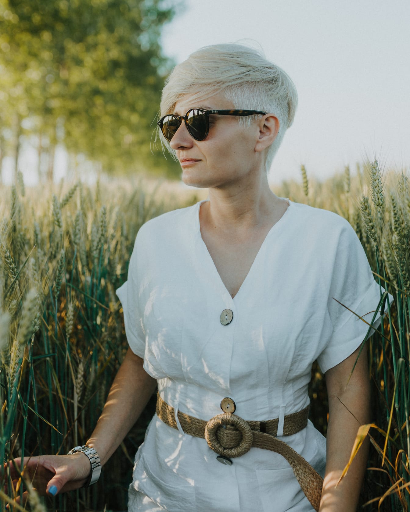 Donna di campagna di bell’aspetto in un campo di grano che indossa abito bianco e occhiali da sole