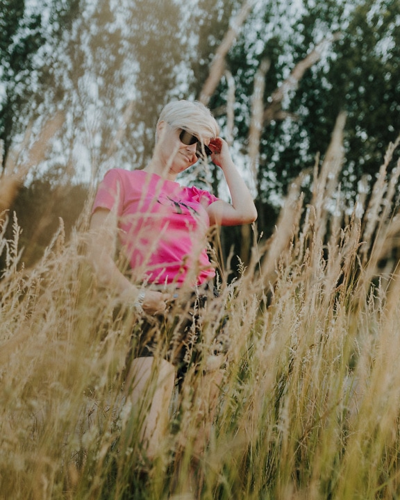 Mujer con pelo rubio corto posando en un campo de hierba alta