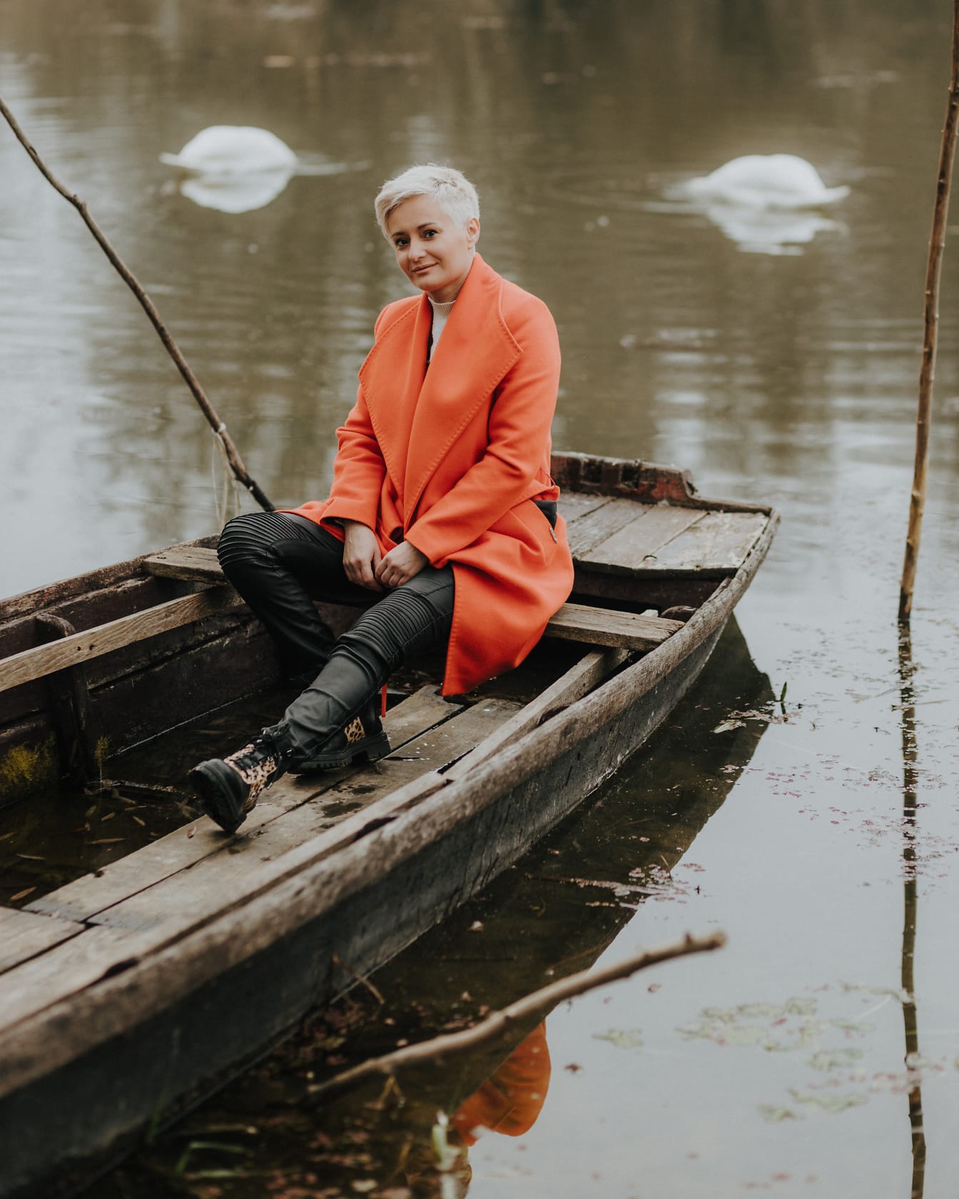 Woman sitting in a boat wearing orange coat and black leather pants and boots