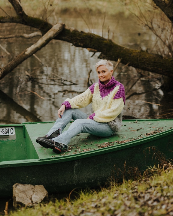 Entzückende blonde Frau in handgemachtem Wollpullover, die auf einem Boot sitzt