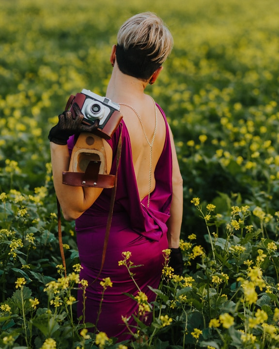Nainen selkänojattomassa mekossa vanhanaikainen analoginen valokuvakamera selässään