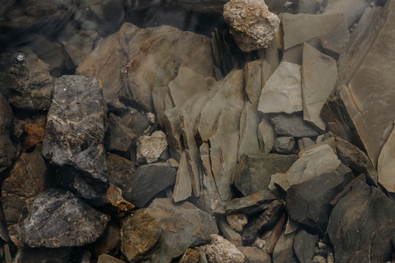 Haufen scharfer Steine unter Wasser auf Flussbett