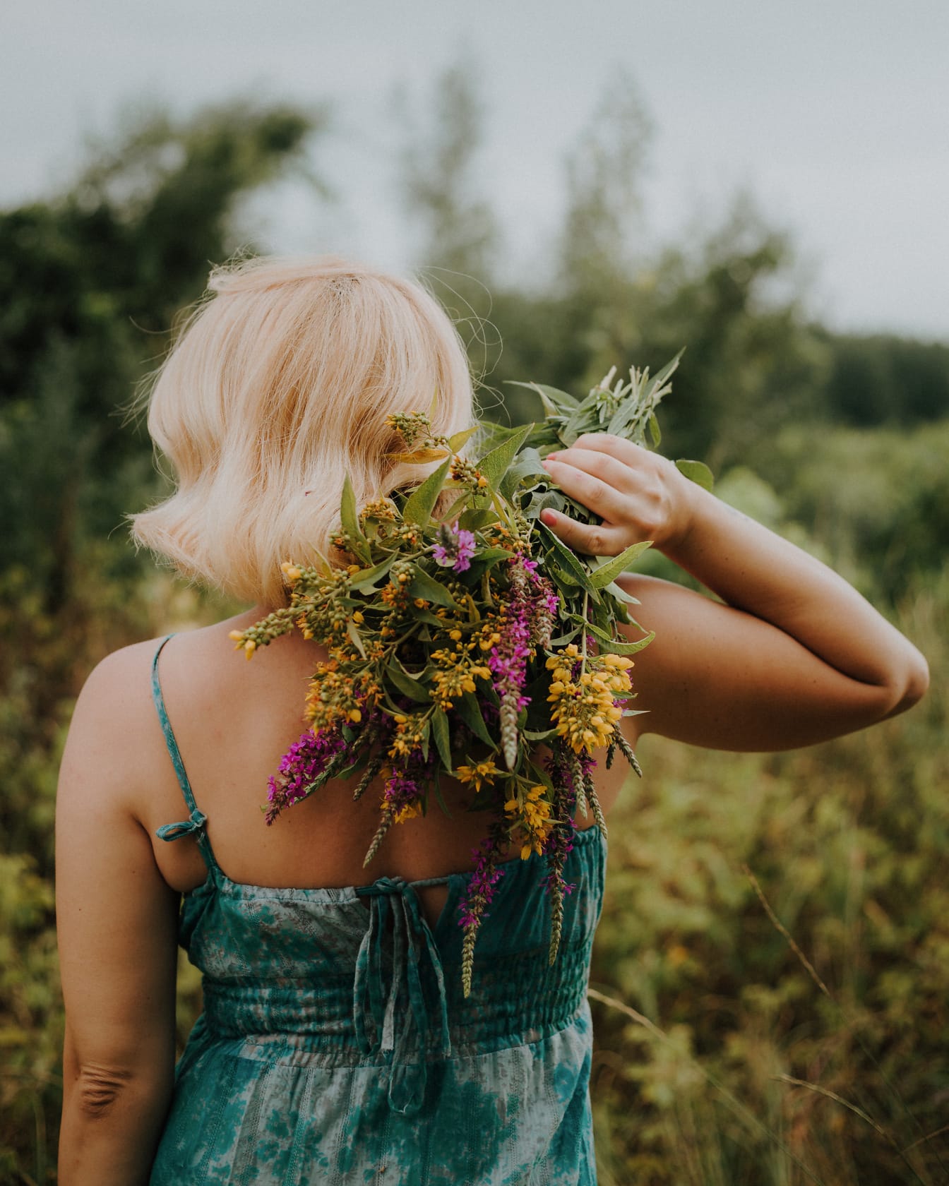 Álló szőke fiatal nő, aki virágcsokrot tart a hátán