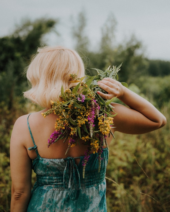 Стояща блондинка млада жена, държаща букет цветя на гърба си