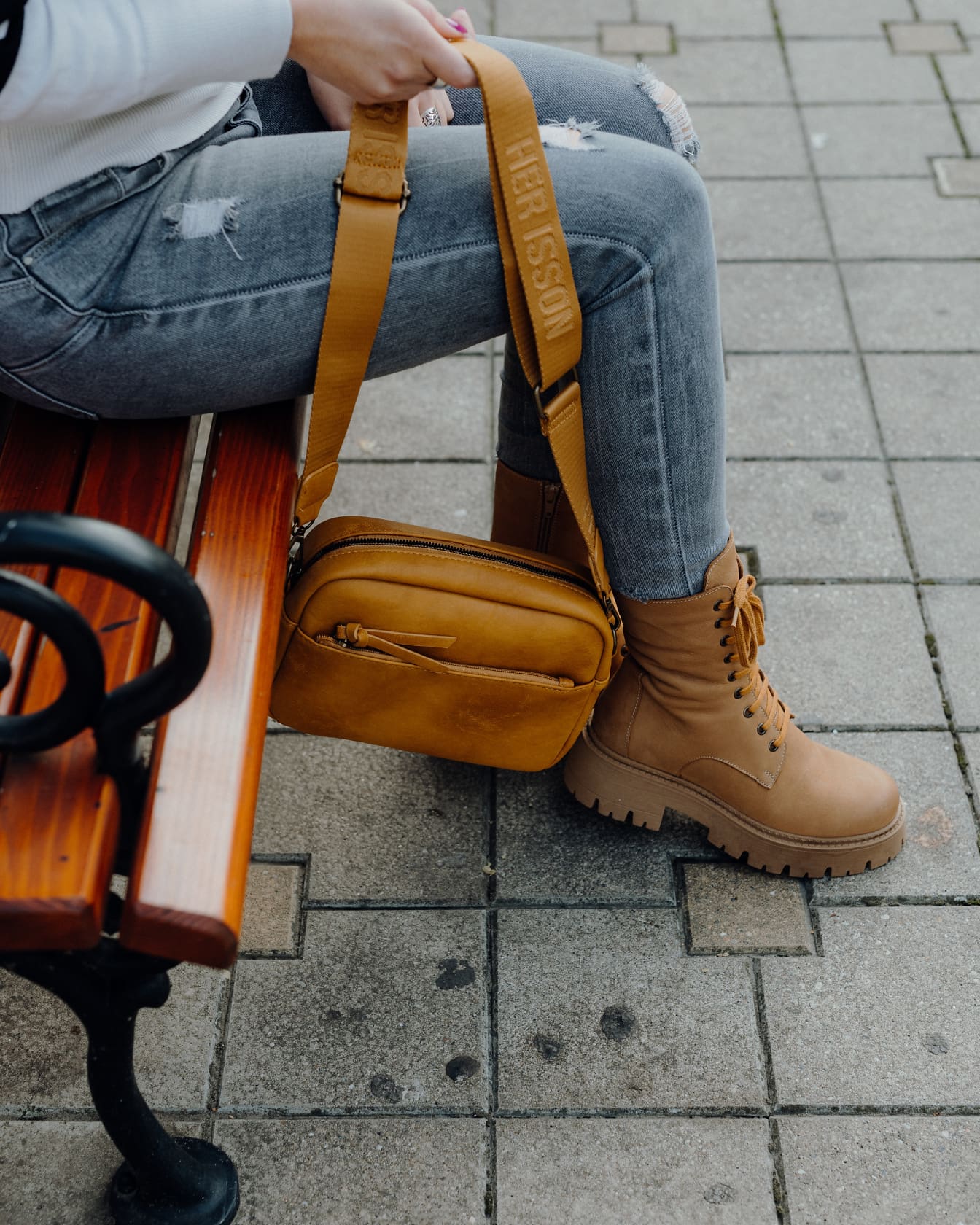 Elinde sarımsı kahverengi deri çanta tutan bir bankta oturan kişi