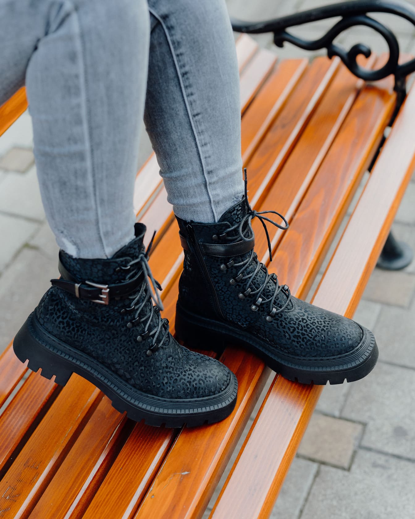 De benen van de persoon in jeansbroek en zwarte moderne laarzen op een houten bank
