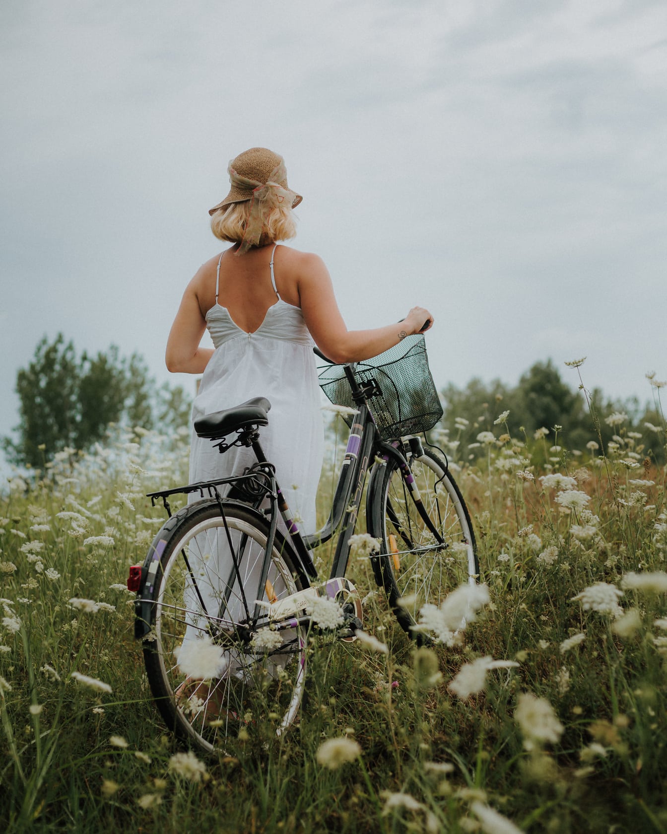 Landsbygda ung kvinne i hvit kjole med sykkel i en blomstereng