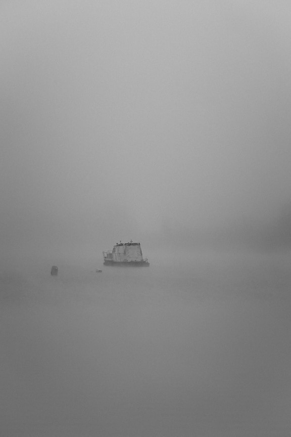 Black and white photo of fishing boat in distance on river in the dense fog