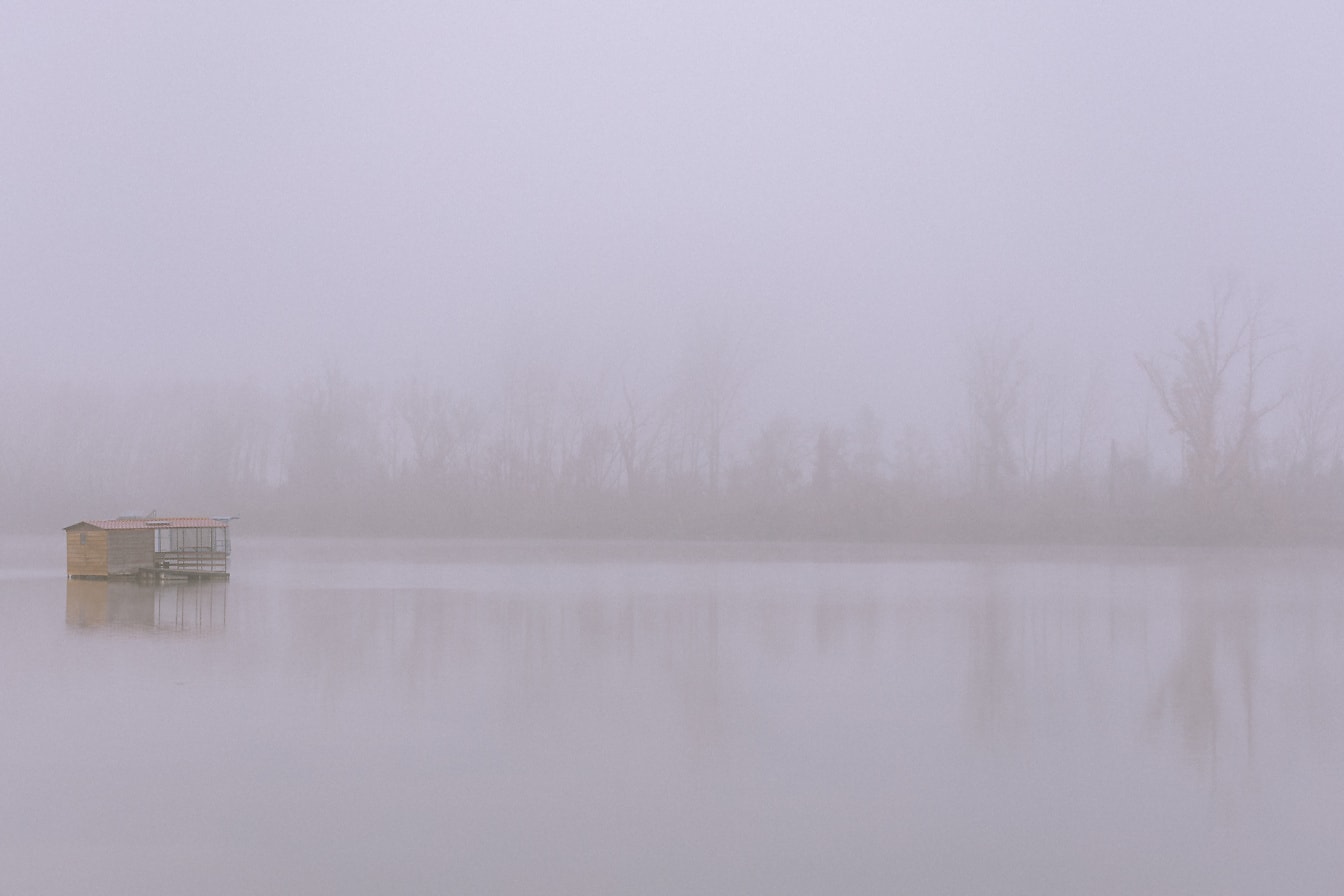 Bootshaus in der Ferne am See bei dichtem Nebel