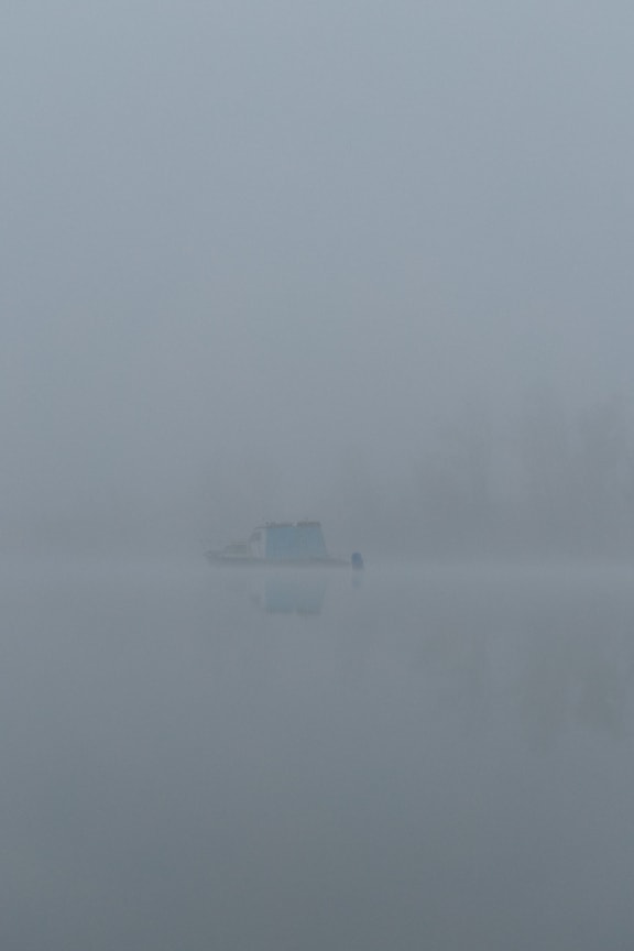 Barco à distância no lago no nevoeiro denso