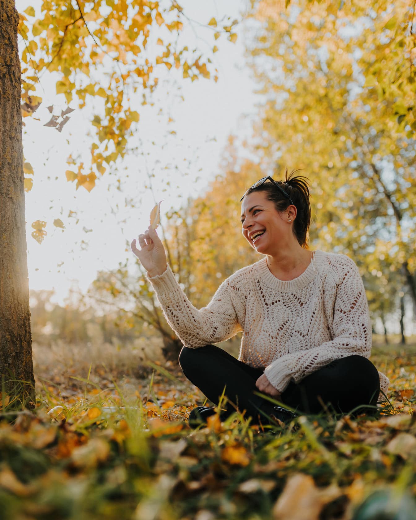Усмихната брюнетка жена седи на земята на открито през есента
