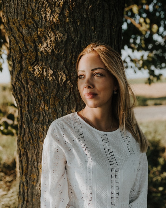Portrait of good looking blonde woman leaning against a tree