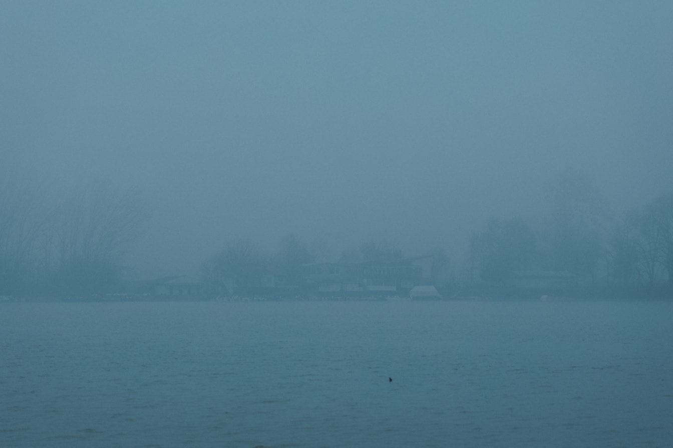 Νερό λίμνης με σιλουέτα σπιτιών σε απόσταση σε πυκνή ομίχλη