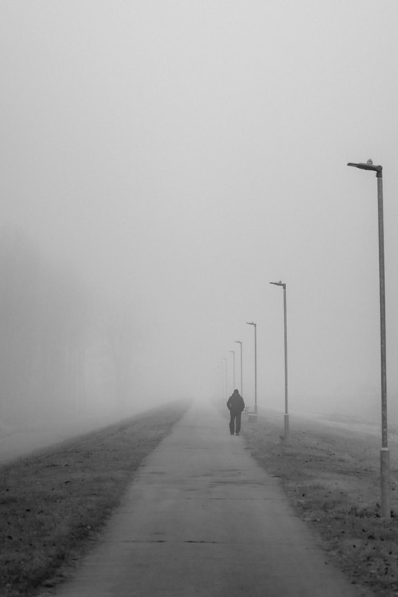 Black and white photo of a man walking on a sidewalk in dense fog
