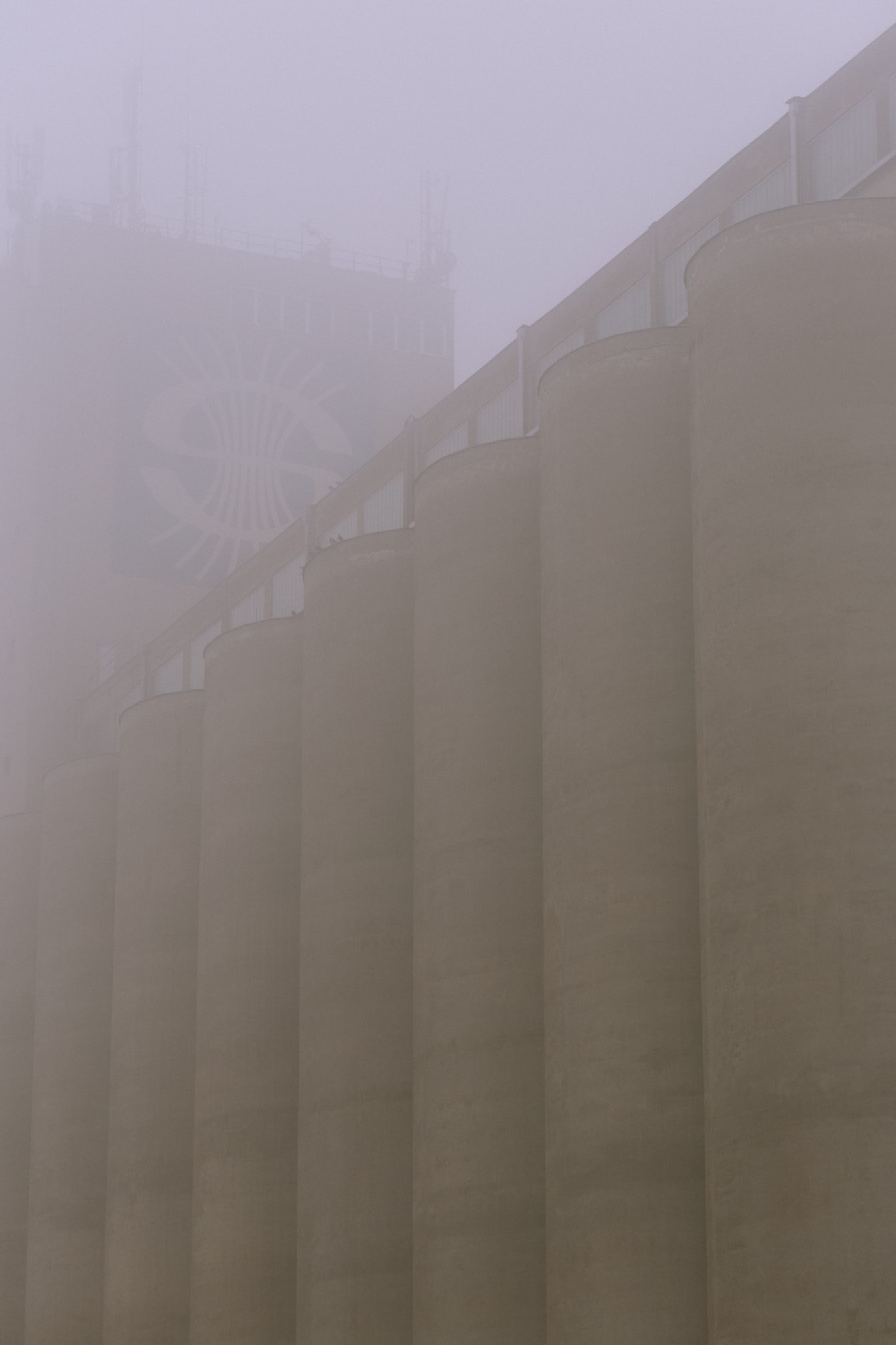 Tall concrete silo building in socialist architectural style in dense fog