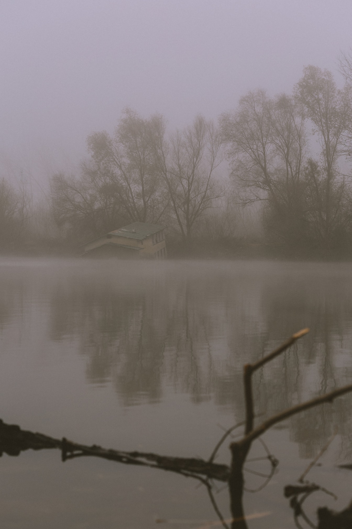 Cobertizo para botes medio inundado en el agua en la orilla de un lago en medio de una densa niebla