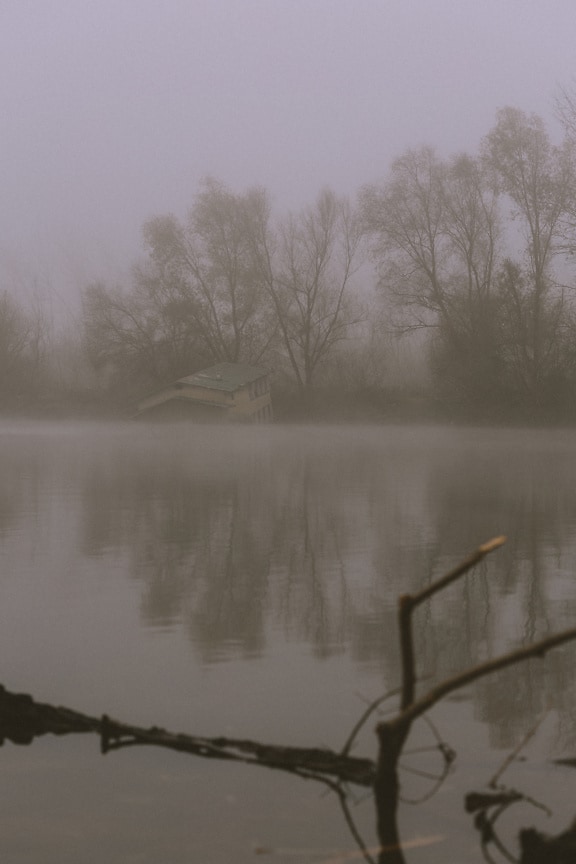 Casa de barco meio inundada na água em um lago em densa neblina