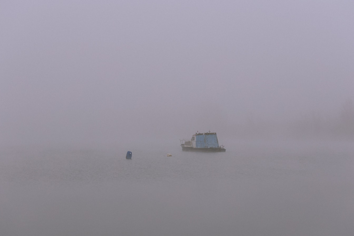 Namodralý malý čln v hustej hmle uprostred jazera