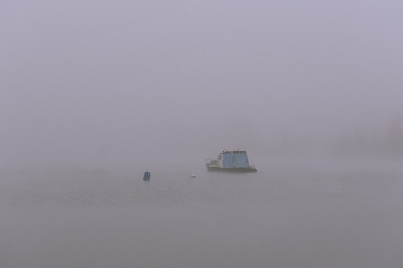 Bluish small boat in the dense fog at the middle of a lake