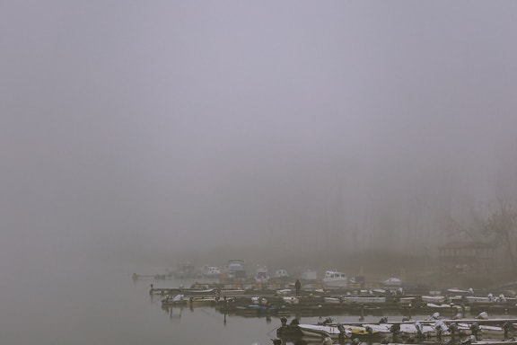 Boats on a lake in dense fog with person standing on harbor