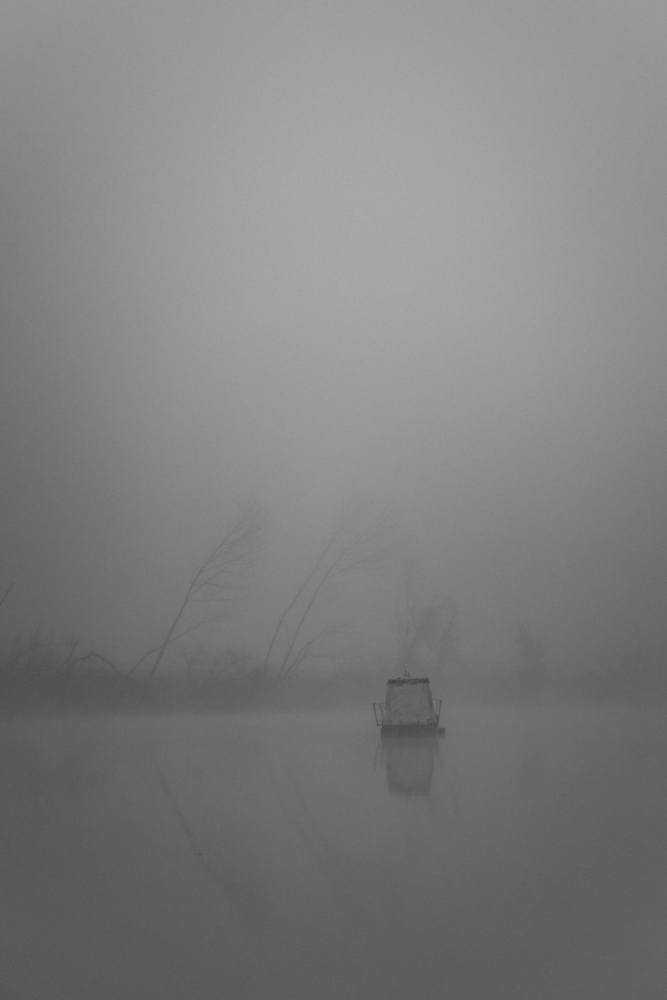 Verticaal georiënteerde zwart-wit landschapsfoto van een boot in de mist