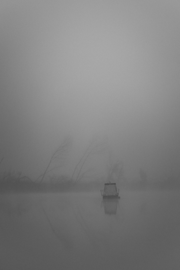 Vertically oriented black and white landscape photo of a boat in the fog