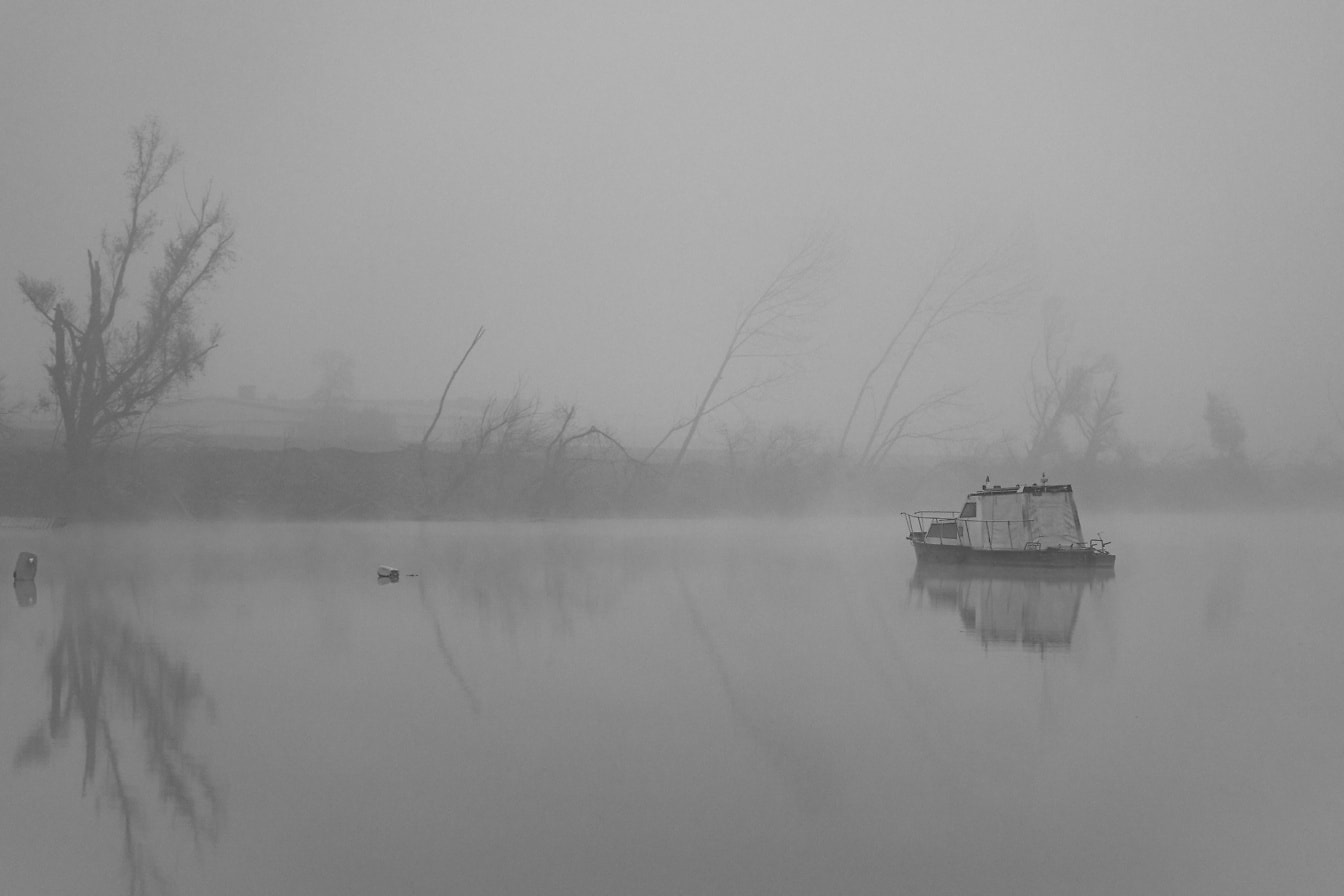 Fotografie alb-negru a unei bărci într-un lac cețos