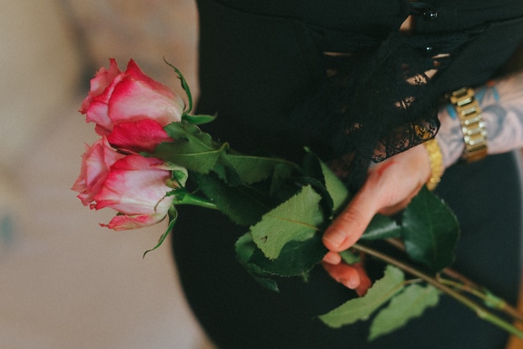 Osoba s potetovanou rukou držící kytici růžových růží