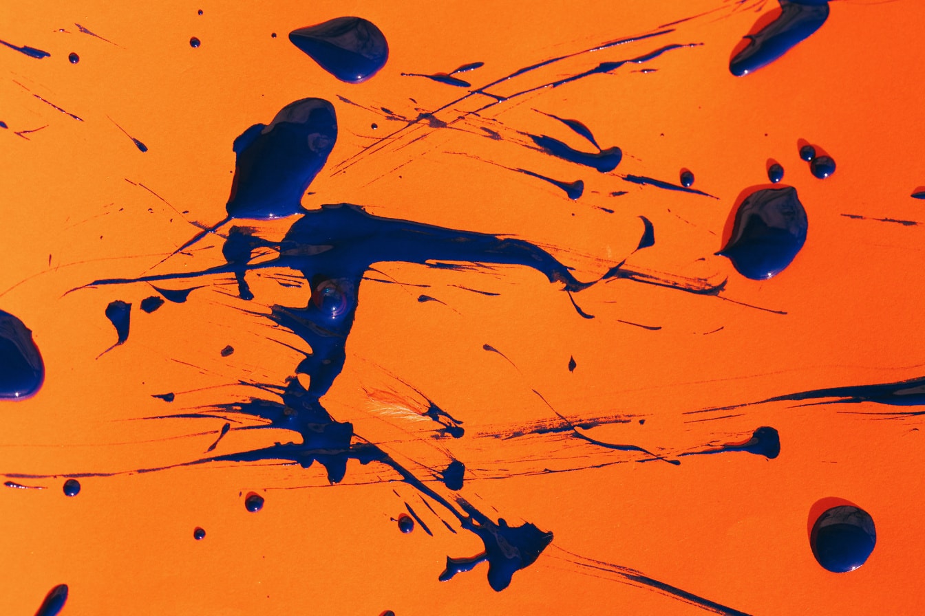 Синя акварелна боя се пръска върху оранжева повърхност
