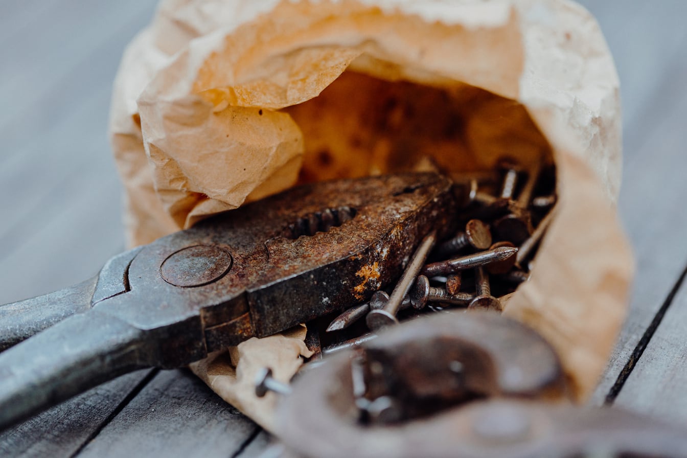 Oude gietijzeren tang en metalen spijkers in een papieren zak
