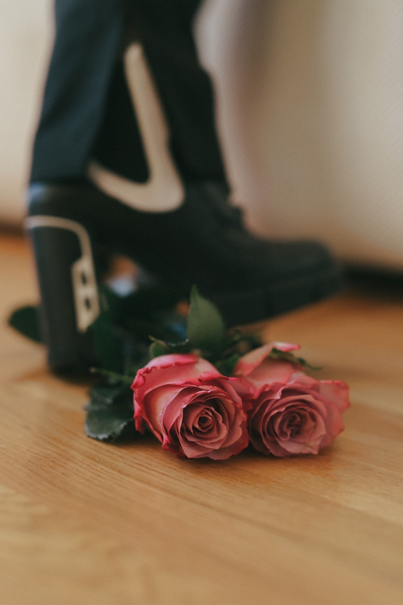 Par lyserøde roser på et trægulv med sko i baggrunden