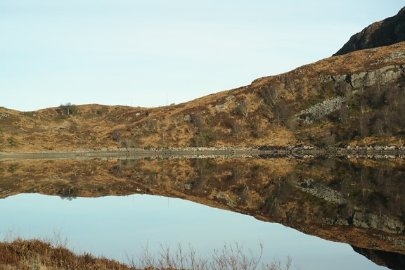 Lago con reflejo de colinas y árboles en la superficie del agua tranquila