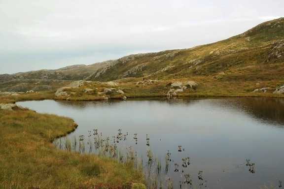 Lago rodeado de hierba y colinas rocosas
