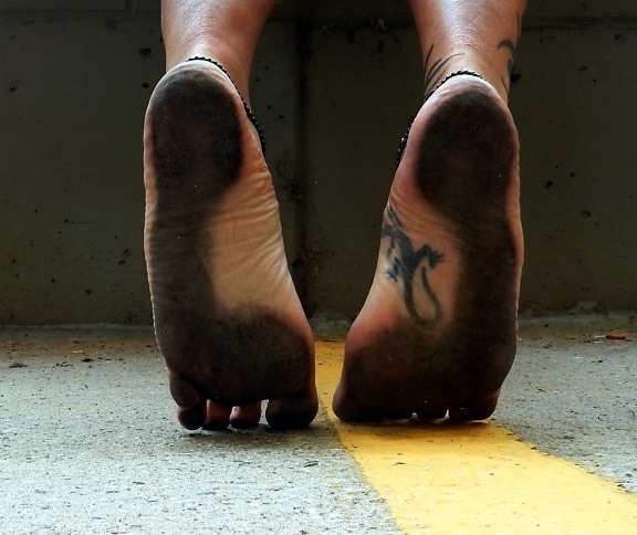 Close-up of a man’s barefoot legs standing on his toes with dirty soles