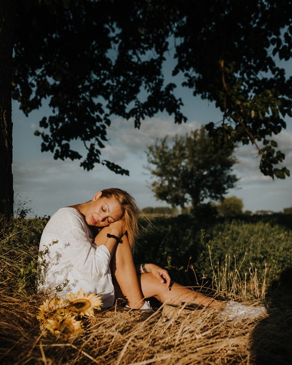 Bonita mujer rubia sentada en un campo y tomando el sol con los ojos cerrados