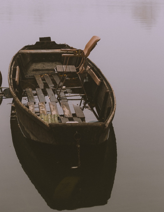 Стара дървена лодка във водата със стол в нея