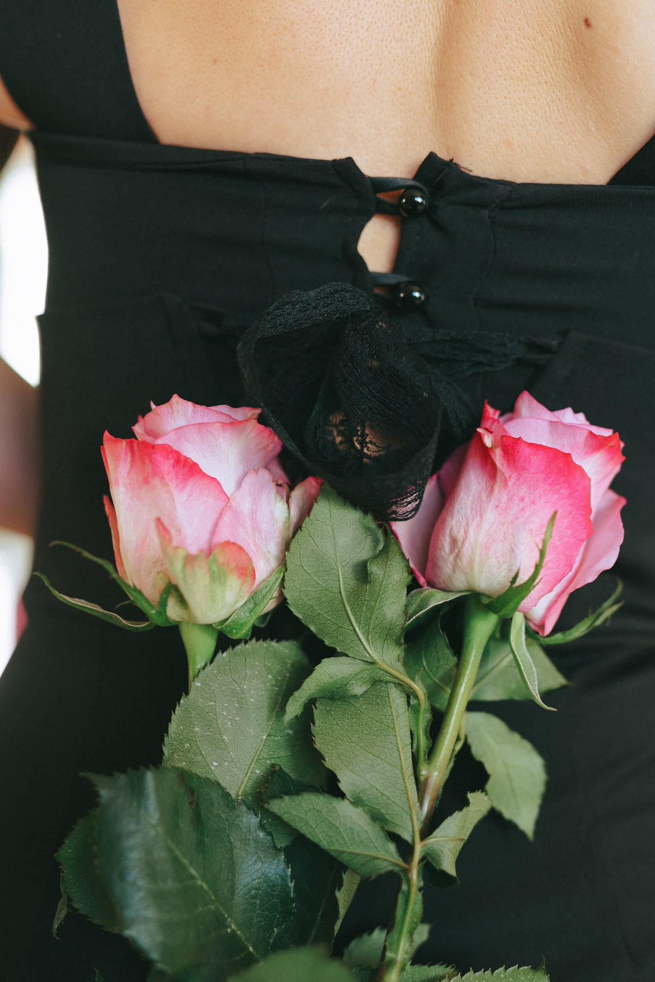Rug van een vrouw die een zwarte kleding met boeket van roze rozen draagt