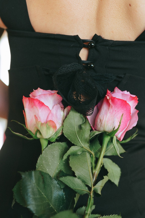 Back of a woman wearing a black dress with bouquet of pink roses