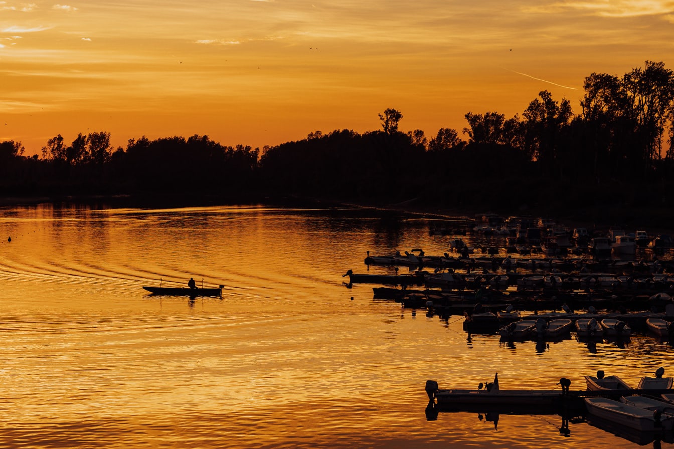 Siluet seorang nelayan di perahu kecil di pelabuhan saat matahari terbenam
