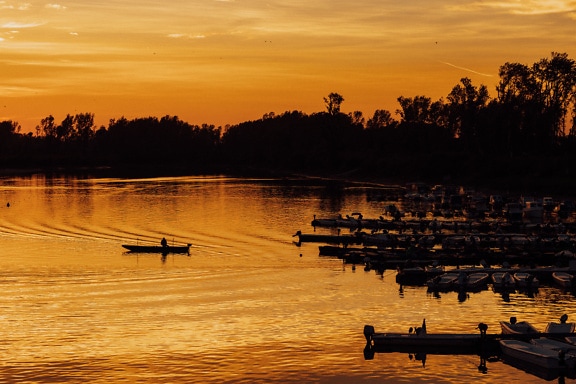Silhouette di un pescatore in una piccola barca in un porto al tramonto